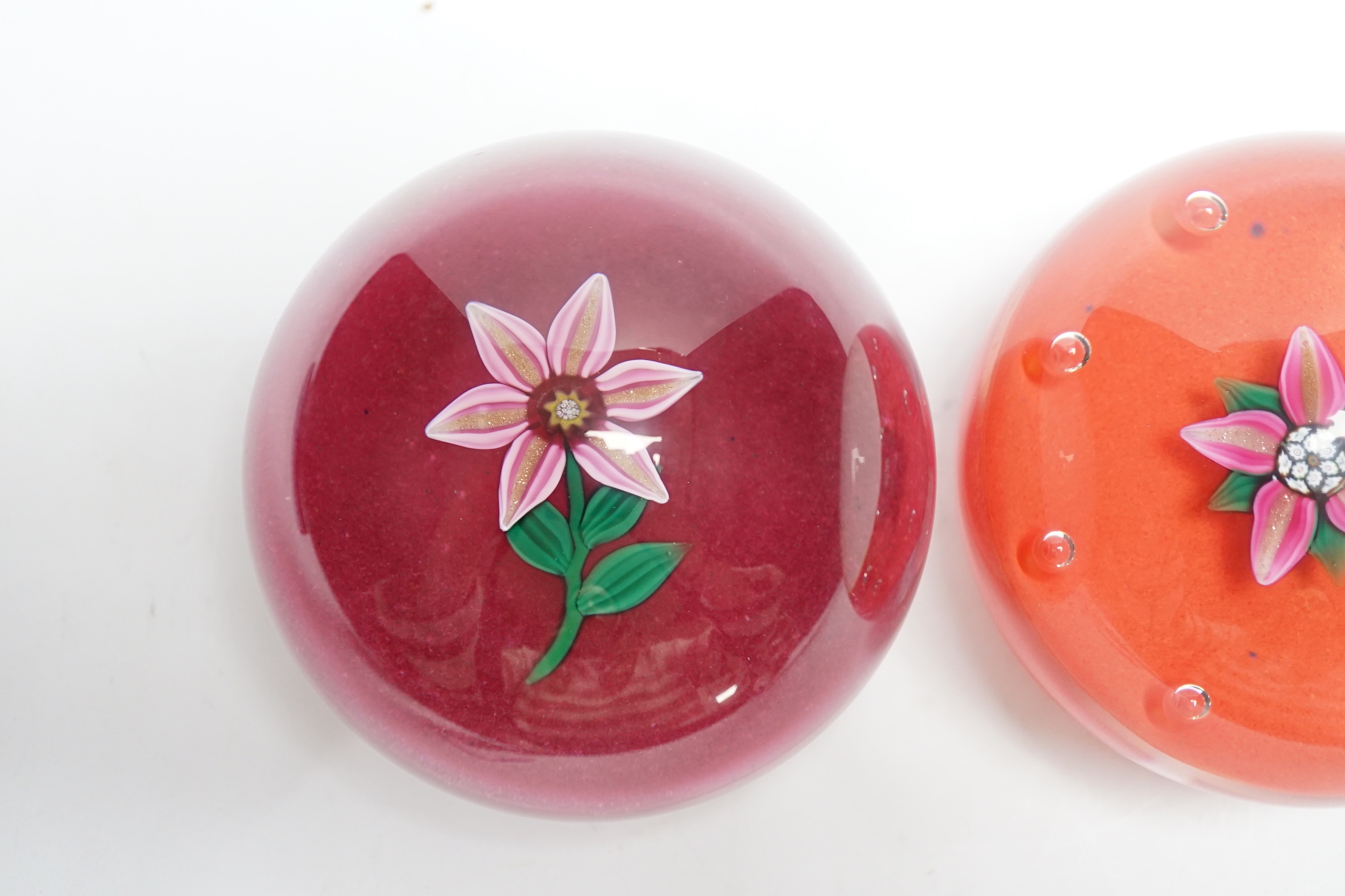 Two Paul Ysart glass ‘flower specimen’ paperweights, both Harland period, the first with a pink and aventurine flower with green stem on a raspberry ground, H cane to base, PY label, 7cm, The second with a pink and adven